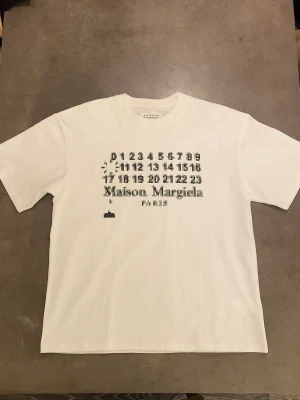 Maison Margiela vit t-shirt med print - Vit t-shirt från Maison Margiela med blurrad logga på framsidan. Knappt använd, storlek L. Kan även passa mindre. Vid fler frågor skicka ett pm!