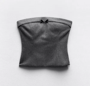 Mörkgrå tubtopp med rosett - Snygg mörkgrå tubtopp i bandeau-modell med liten svart rosett framtill. Toppen har en stilren och enkel design, perfekt att matcha med både jeans och kjol. Materialet känns mjukt och följsamt mot huden.