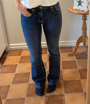 mörkblå bootcut jeans - Säljer ett par jeans i mörkblå tvätt med klassisk bootcut passform. Jeansen har fem fickor, knapp och dragkedja framtill samt snygga kontrastsömmar. Perfekt för dig som gillar retrovibbar och tidlös stil. (Storlek S full längd) 