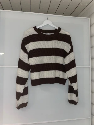 Randig stickad tröja - Säljer en stickad tröja från H&M Divided i storlek S. Tröjan har breda horisontella ränder i mörkbrunt och vitt, rund hals och lång ärm. Modellen är lite croppad och har en loose passform, perfekt för att styla med skjorta under eller bara som mysig vintertröja☺️OBS! Dock se en liten defekt.