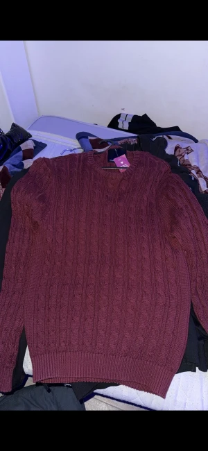 Vinröd kabelstickad tröja - Snygg vinröd kabelstickad tröja med rund hals och långa ärmar. Tröjan har ett klassiskt mönster och ribbade muddar vid ärmslut och nederkant. Perfekt för dig som gillar en chill och stilren look under höst och vinter.