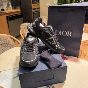 Svarta Dior B30 sneakers - Säljer ett par svarta Dior B30 sneakers med coola vita detaljer och reflekterande inslag. Skorna har en chunky sula, mesh och syntetpaneler, samt snörning framtill. Märkets logga syns på sidan och plösen. Perfekt för dig som gillar exklusiv streetstyle. Säljer då dem vart för små för mig.