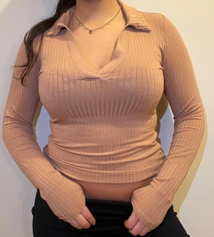 Beige ribbad långärmad polotopp - Säljer en beige ribbad polotopp med lång ärm och v-ringad krage. Toppen har en slim passform och är tillverkad i mjukt, stretchigt material som sitter snyggt på kroppen. Perfekt för dig som gillar en clean och stilren look med lite edge. Storlek S Använd men väldigt god skick!   Obs! Modellens längd är 162.