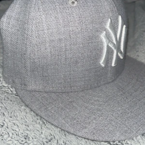 Grå New Era Yankees keps 59FIFTY - Pris går o diskutera Helt ny aldrig använd. Snygg grå New Era 59FIFTY keps med New York Yankees-logga i vitt broderi framtill. Kepsen har en klassisk rak skärm och MLB-logga baktill. Materialet är 80% akryl och 20% ull, vilket ger en mjuk och bekväm känsla. Perfekt för dig som gillar streetstyle och sport.