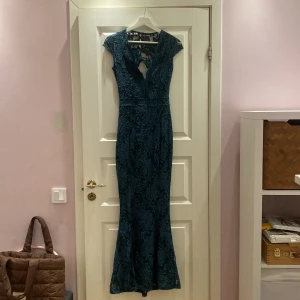 Blå spetsklänning från Bubbleroom - Säljer en lång grön spetsklänning från Bubbleroom i storlek 34. Klänningen har v-ringning, blommigt spetsmönster, knappar i ryggen och en snygg öppen ryggdetalj. Passformen är slim och ärmarna är korta. Perfekt för dig som vill sticka ut med en elegant look.