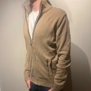 Stickad cardigan  - Stickad cardigan ifrån Dressmann. Storleken är S och färgen är Beige. Modellen är 176cm och väger 65kg. Skriv för mer information ✅