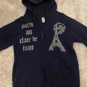 Mörkblå hoodie med strass och Eiffeltorn - En fet marinblå hoodie perfekt för en vanlig skoldag eller om man bara ska vara hemma. Det står 'paris au clair de lune' vilket betyder Paris i månets sken tror jag. Den är xs och exakt 60cm borde passa någon som är mellan 160-170 ish. Perfekt får både killar och tjejer