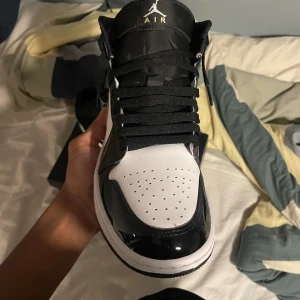Nike Air Jordan 1 svart/vit/silver - Säljer ett par Nike Air Jordan 1 i svart, vitt och silver med glansiga detaljer. Klassisk high-top siluett, svart snörning och perforerad tå. Swoosh-logga på sidan och Jumpman-logo på plösen. Riktigt snygga sneakers för dig som vill sticka ut.