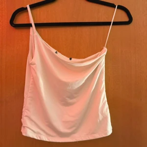 Vit linnetopp med ett axelband - Säljer en stilren vit linnetopp med ett tunt axelband och snygg draperad halsringning. Perfekt för varma dagar eller att styla lager på lager. Enkel och clean design som är lätt att matcha med olika outfits.