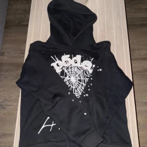 Svart Sp5der Hoodie - Svart Sp5der hoodie med vitt puff print. Tröjan har huva och är bomull med fleece på insidan. Perfekt för dig som gillar streetwear och unika detaljer.
