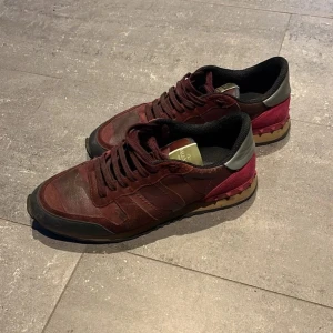 Valentino Rockrunner vinröda sneakers - Snygga Valentino Rockrunner sneakers i vinrött skinn och mocka med svarta och grå detaljer. Skorna har klassisk snörning, mönstrad sula och ikoniska nitar baktill. Perfekta för dig som vill sticka ut med exklusiva och trendiga sneakers. Tveka inte att skriva vid frågor eller för fler bilder. Kan tänka mig att gå ner i pris vi smidig affär.