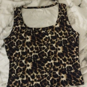 Leopardmönstrad ärmlös topp XL - Säljer en ärmlös topp i storlek XL med leopardmönster i bruna, svarta och beige toner. Toppen har breda axelband och fyrkantig ringning. Tillverkad i stretchigt material av 95% polyester och 5% elastan. Perfekt för dig som vill sticka ut med ett djurmönster.