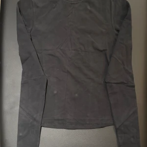 Svart långärmad tröja från SKIMS storlek S - En enkel svart långärmad tröja från SKIMS i storlek S. Tröjan har rund halsringning och är gjord i mjuk bomull, perfekt för att bygga lager eller ha som basplagg. Stilren och lätt att matcha med andra kläder.