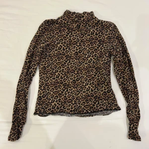 Leopardmönstrad polotopp med lång ärm - Säljer en snygg polotopp med leopardmönster i bruna och svarta toner. Toppen har lång ärm och en hög krage som ger en cool vibe. Materialet känns mjukt och stretchigt 