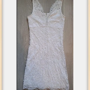 Fin Vit spetsklänning från Cubus/XS/S - Säljer en vit kortklänning från Cubus med v-ringad hals och breda axelband. Klänningen är täckt av blommig spets och har en dragkedja i ryggen. Materialet är en mix av nylon, viskos och polyester, vilket gör den mjuk och följsam. Perfekt för alla tillfällen!Oanvänd!!!!! 