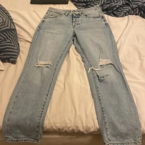 Ljusblå jeans från 157, straight fit - Säljer ett par ljusblå jeans från 157 i straight fit med slitna detaljer och hål på båda knäna. Klassisk femficksmodell med knapp och dragkedja framtill. Jeansen har normal passform och är tillverkade i bomull. Perfekt för dig som gillar en avslappnad och trendig look.