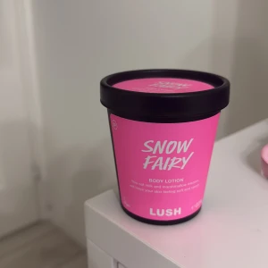 Lush Snow Fairy Body Lotion 225g - Lush Snow Fairy Body Lotion i en rosa plastburk med svart lock. Doftar sött av marshmallow och godis, innehåller mandelolja, jojobaolja och kakaosmör för mjuk hud. Perfekt för dig som älskar färgstarka och lekfulla produkter.