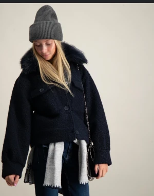 Svart teddyjacka med fluffig krage - Säljer en svart teddyjacka med stor, fluffig fuskpäls-krage. Jackan är croppad och har två bröstfickor med knappar framtill. Materialet är mjukt och ger en cool, trendig vibe. Perfekt för dig som gillar att sticka ut med din stil.Nästan helt ny.Priset går att diskuteras vid snabb köp .