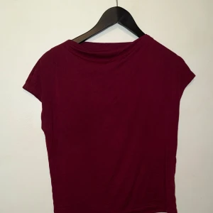 Vinröd enkel topp med kort ärm - Säljer en vinröd topp med korta ärmar och rund hals. Modellen är rak och enkel, perfekt för att matcha med olika stilar. Tunt och mjukt material som känns skönt mot huden.