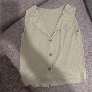 Ljusbeige väst med knappar - Snygg ljusbeige topp med klassisk krage och fem knappar framtill. Toppen är ärmlös och har en rak, loose passform som gör den enkel att styla. Tillverkad i mjukt bomullsmaterial för en skön känsla. Perfekt för dig som gillar minimalistisk och clean look.