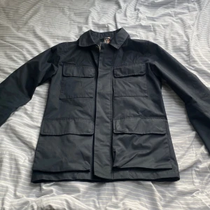 Mörkblå overshirt/jacka från Dressmann S - Ny pris 1500kr. Stilren mörkblå overshirt från Dressmann med fyra stora fickor framtill, dragkedja och knappar. Klassisk krage och rak passform, perfekt för lager-på-lager. Tillverkad i bomull och polyester för en lätt känsla. Skriv om du har nån fråga och ge gärna prisförslag 