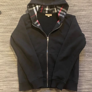 Svart Burberry hoodie med rutig huva - Säljer en snygg burberry hoodie! Hoodien är i mycket bra skick och har inga defekter. Perfekt hoodie nu till kallare väder! Om ni har några frågor så är de bara att höra av er😊