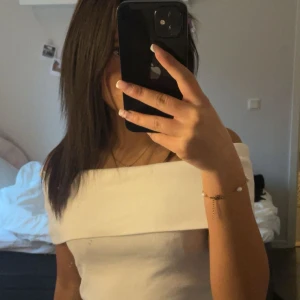 Vit offshoulder croppad topp - Säljer en vit offshoulder topp med croppad passform. Toppen har en bred kant över axlarna storlek xs från bik bok 