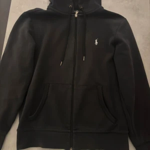 Svart hoodie från Polo Ralph Lauren XS - Svart hoodie från Polo Ralph Lauren i storlek XS. Klassisk design med dragkedja, huva med snörning och två fickor framtill. Använd bara fåtalet gånger, 9/10 skick 