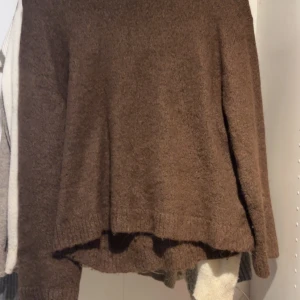Brun stickad tröja med lång ärm - Mysig brun stickad tröja med lång ärm och avslappnad passform. Perfekt för kyliga dagar och enkel att matcha med jeans eller leggings. Tröjan har en klassisk rund hals och ribbade muddar vid ärmslut och nederkant.
