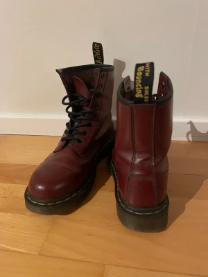 Vinröda Dr. Martens 1460 boots - Säljer ett par klassiska Dr. Martens 1460 boots i vinrött skinn med svart snörning och rund tå. Ikonisk gul söm runt sulan och dragflik med logga bak. 