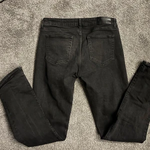 Svarta jeans - Svarta dressman jeans med slim passform och klassisk femficksdesign. Jeansen har raka ben, knapp och dragkedja i gylfen. Materialet är mjukt jeans med lite stretch för extra komfort. Jeansen är knappt använda och köpta direkt i butik för 600kr. Hör av dig vid funderingar!