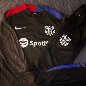 Svart FC Barcelona Nike fotbollstracksuit - Snygg svart FC Barcelona tracksuit från Nike med klubbmärke och Spotify-logga på bröstet. Storleken är M men passar S, kom dm för fler frågor och bilder !