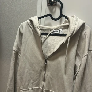 Beige hoodie med dragkedja från Weekday - Säljer en beige hoodie från Weekday med dragkedja framtill och huva med snörning. Tröjan har långa ärmar och mjukt fleecefoder på insidan. Perfekt för chill dagar och enkel att matcha med jeans eller mjukisbyxor.