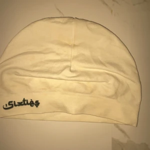 Vit mössa från Sixties - Vit mössa från Sixties med svart logga tryckt framtill. Enkel och clean design med rundad form och bred kant nedtill. Tillverkad i mjuk bomull som känns skön mot huvudet. Perfekt för dig som gillar minimalistisk stil och vill ha en basic mössa.