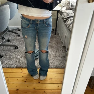 Blå bootcut jeans  - Säljer ett par blå bootcut jeans med låg midja och slitna detaljer vid knäna och fickan. Jeansen har dubbla knappar i midjan, klassiska fickor och passformen är loose. Storlek 36💖🩷🩷