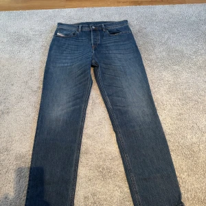 Blå jeans från Diesel W31 - Snygga blå jeans från Diesel i klassisk straight fit med fem fickor och diskreta slitningar. Jeansen har normal passform och är tillverkade i slitstarkt denim med en cool Diesel Industry-lapp bak i midjan. Perfekt för dig som gillar tidlös stil.