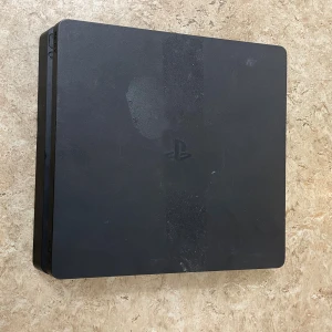 PlayStation 4 Slim - Sony PlayStation 4 Slim i svart. Konsolen har synliga märken och ytslitage på ovansidan, men är i fullt fungerande skick. Perfekt för dig som vill spela populära PS4-titlar till ett bra pris. Strömkabel och handkontroller ingår ej.