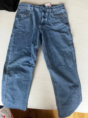 Blå jeans från LMTD i storlek 14S - Snygga blå jeans från LMTD i klassisk femficksmodell. Jeansen har rak passform och normal midja, med tydliga sömmar och bälteshällor. Perfekta för dig som gillar en enkel och tidlös stil. Materialet är slitstarkt denim i bomull. Använts som baggy jeans. 
