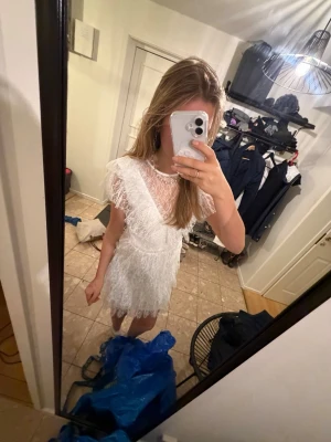 Vit spetsklänning med volanger - Superfin vit kort klänning i spets med flera lager volanger och v-ringad detalj framtill. Klänningen har korta ärmar och är genombruten i spetsmaterial, vilket ger en romantisk och luftig känsla. Perfekt för sommarens alla tillfällen!