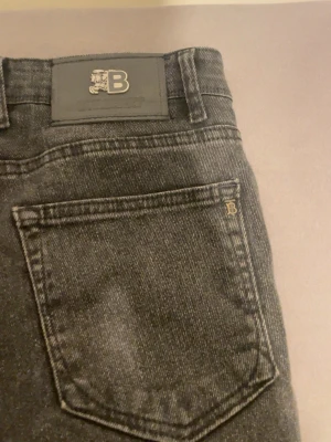 Burberry svarta regular fit W33/L34 - Svarta från Burberry, modell 5527, med snygga röda sömmar och klassisk Burberry-logga på bakfickan. Jeansen har knappgylf och är tillverkade i 99% bomull för en skön och slitstark känsla. Perfekt för dig som gillar stilrena och tidlösa jeans.