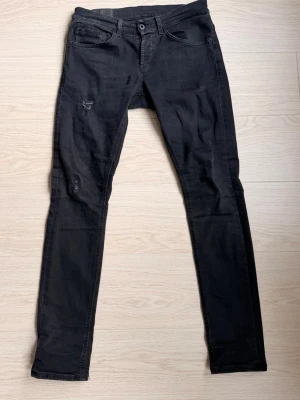 Svarta jeans från Dondup - Svarta jeans från Dondup i modelen George, klassisk femficksdesign. Jeansen har diskreta slitningar på framsidan och en liten Diesel-logga på bakfickan. Materialet är mjukt och stretchigt jeans, perfekt för en avslappnad och cool look.