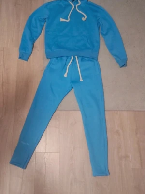 Blå mjukisbyxor från 0% Fuckeries - Blå mjukisbyxor från 0% Fuckeries med vit snörning i midjan och ett stort graffiti-inspirerat tryck på baksidan. Byxorna har slim passform och är gjorda i mjukt bomullsmaterial, perfekta för chill eller träning.