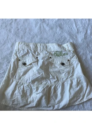 Vit cargokjol  - Säljer en vit cargo kortkjol från Peak Performance med cool broderad logga i grönt på bakfickan. Storlek S. 