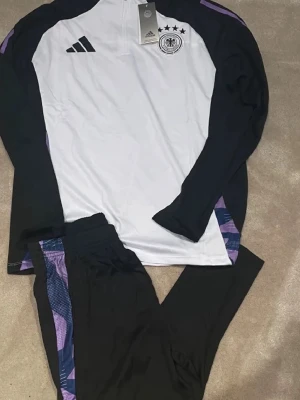 DFB träningsset  - Bilden visar ett träningsset från Adidas med långärmad tröja och byxor, men inga skor syns på bilden.