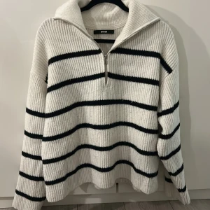 Vit och svart randig stickad tröja Bikbok - Säljer en ribbstickad tröja från Bikbok i storlek S. Tröjan är vit med svarta horisontella ränder, har lång ärm och en hög krage med half zip-dragkedja framtill. Modellen är loose fit och passar perfekt för kyliga dagar. Lite nopprig!
