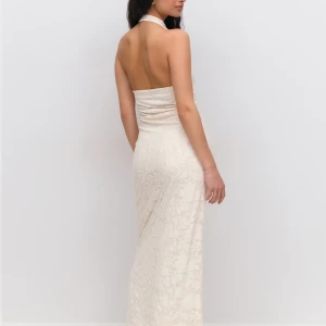 Vit långklänning  - Säljer en elegant vit långklänning med halterneck och öppen rygg. Klänningen har ett subtilt blommigt mönster i tyget och är figurnära med en mjuk drapering vid halsen. Perfekt för sommarens speciella tillfällen.