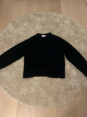 Mörkblå stickad tröja från Gina Tricot - En mörkblå, klassisk stickad tröja från Gina Tricot i ullblandning. Tröjan har rund hals och långa ärmar med ribbade muddar. Tröjan ser svart ut på bilden men det är ljuset. Storlek xs. Köptes för 3 månader sen för cirka 400 kr. Har knappt använts sen dess.