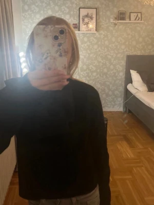 Svart stickad tröja med rosett - Snygg svart stickad tröja med lång ärm och stor rosett på axeln. Tröjan har en klassisk rund hals och är perfekt för dig som gillar stilrena detaljer. Passar till jeans eller kjol och har en skön loose fit.