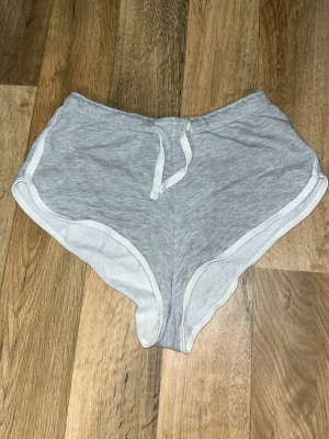 Grå shorts med snörning - Säljer ett par grå shorts med vit kant och snörning i midjan. De har en loose passform och är tillverkade i mjuk bomull, perfekta för chill dagar eller träning. Har en elastisk midja för extra komfort. Köpt från New Yorker och använda ett flertal gånger