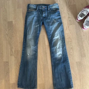 Diesel bootcut jeans - Supersnygga jeans från diesel i blå tvätt med snygga slitningar och bootcut-ben. Jeansen har fem fickor, knappgylf och är tillverkade i robust denim. Perfekt för dig som gillar retrostil och vill ha ett par jeans med karaktär. Storlek w28 L32